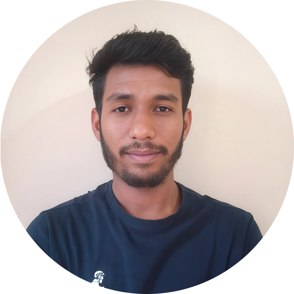 A young man with short dark hair and a beard, wearing a navy blue shirt, poses in front of a plain light-colored background.